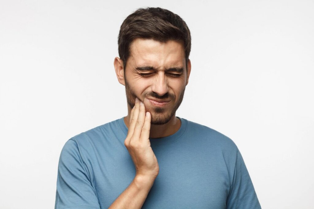 A man grimacing and holding his jaw, indicating toothache or pain.