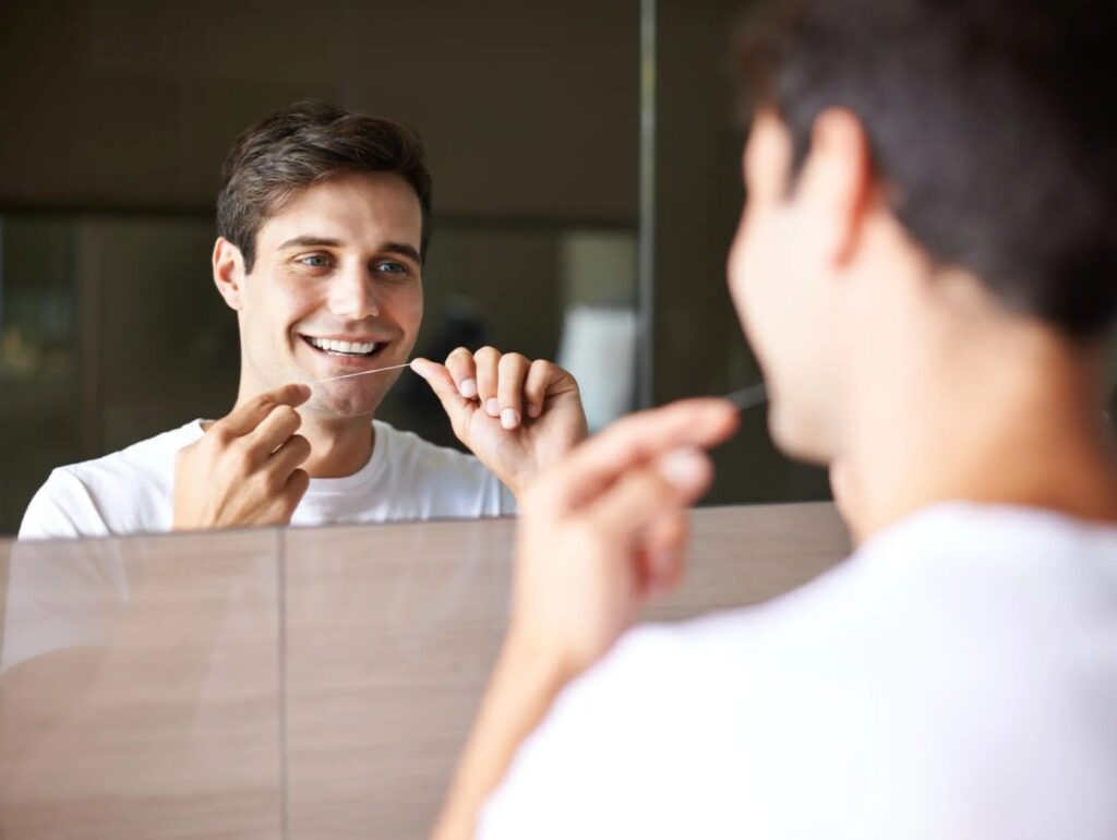 a man is flossing his teeth in front of a mirror .