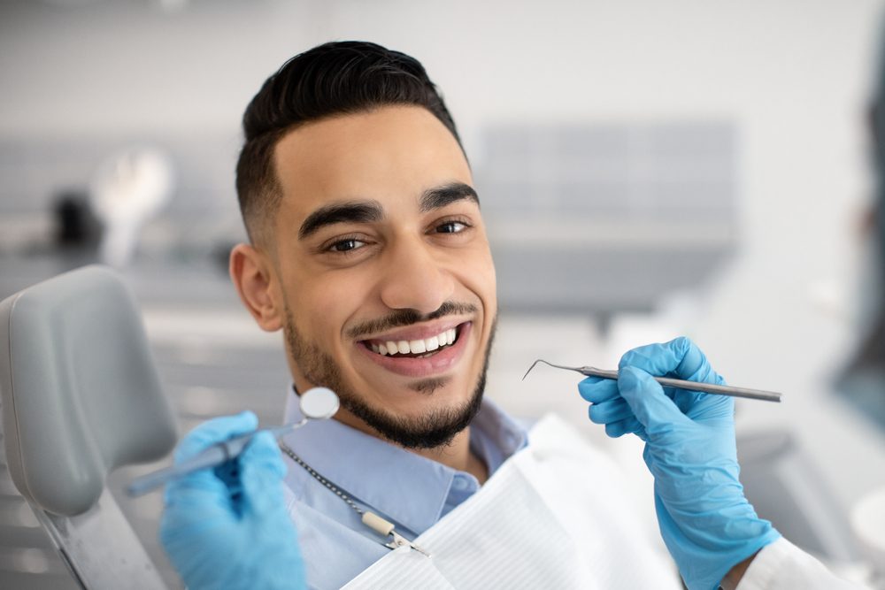 Man with a bright smile in a dental chair, holding dental tools.