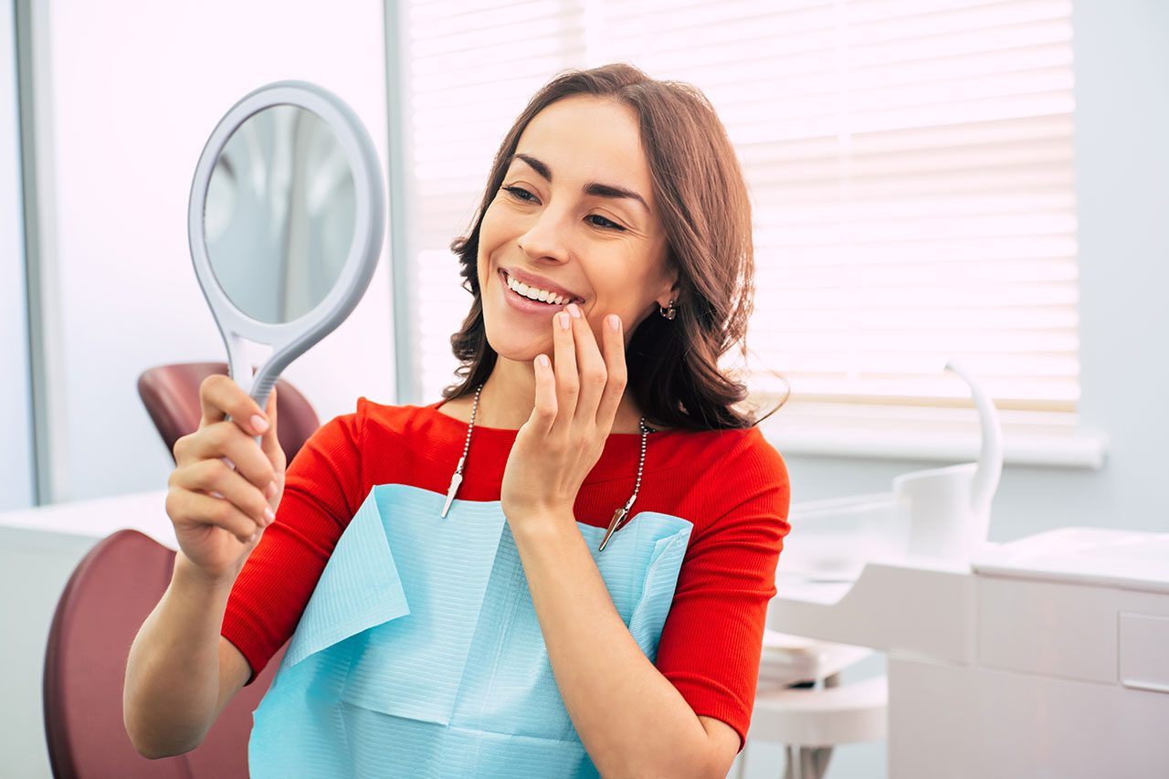 una mujer se está mirando los dientes en un espejo en el dentista.