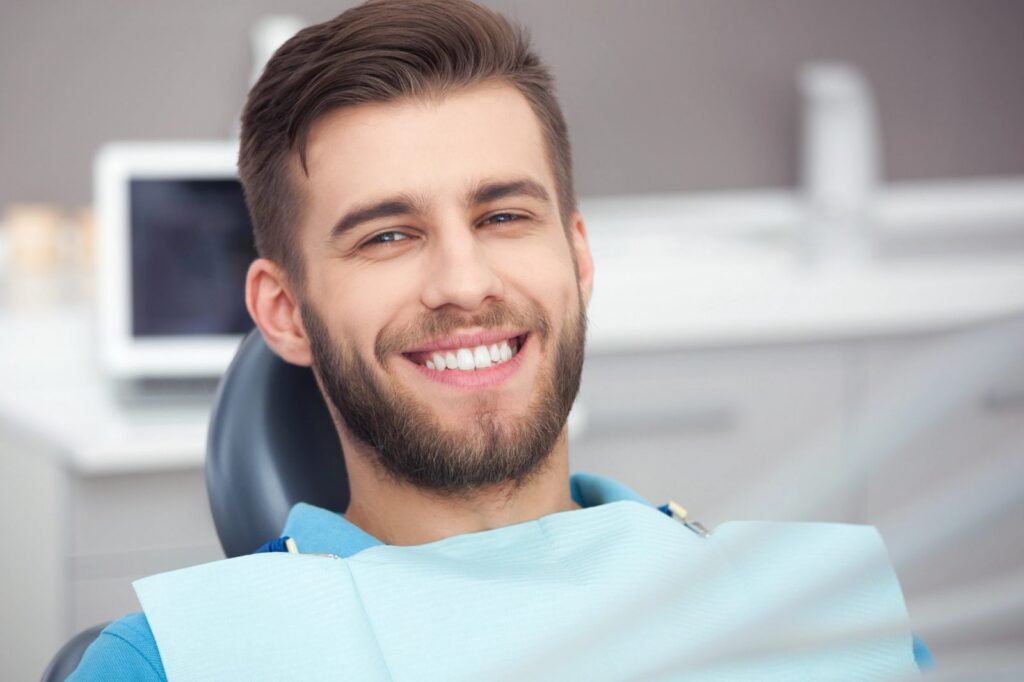 A man with a beard smiles, showing white teeth, in a dental chair.