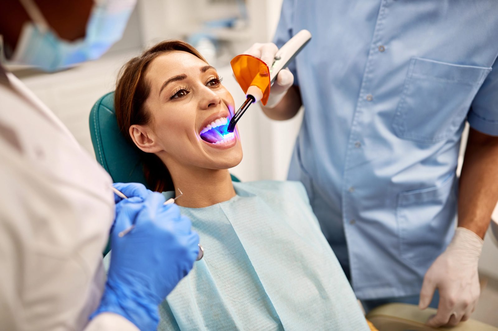 una mujer está sentada en una silla dental recibiendo blanqueamiento dental de un dentista.