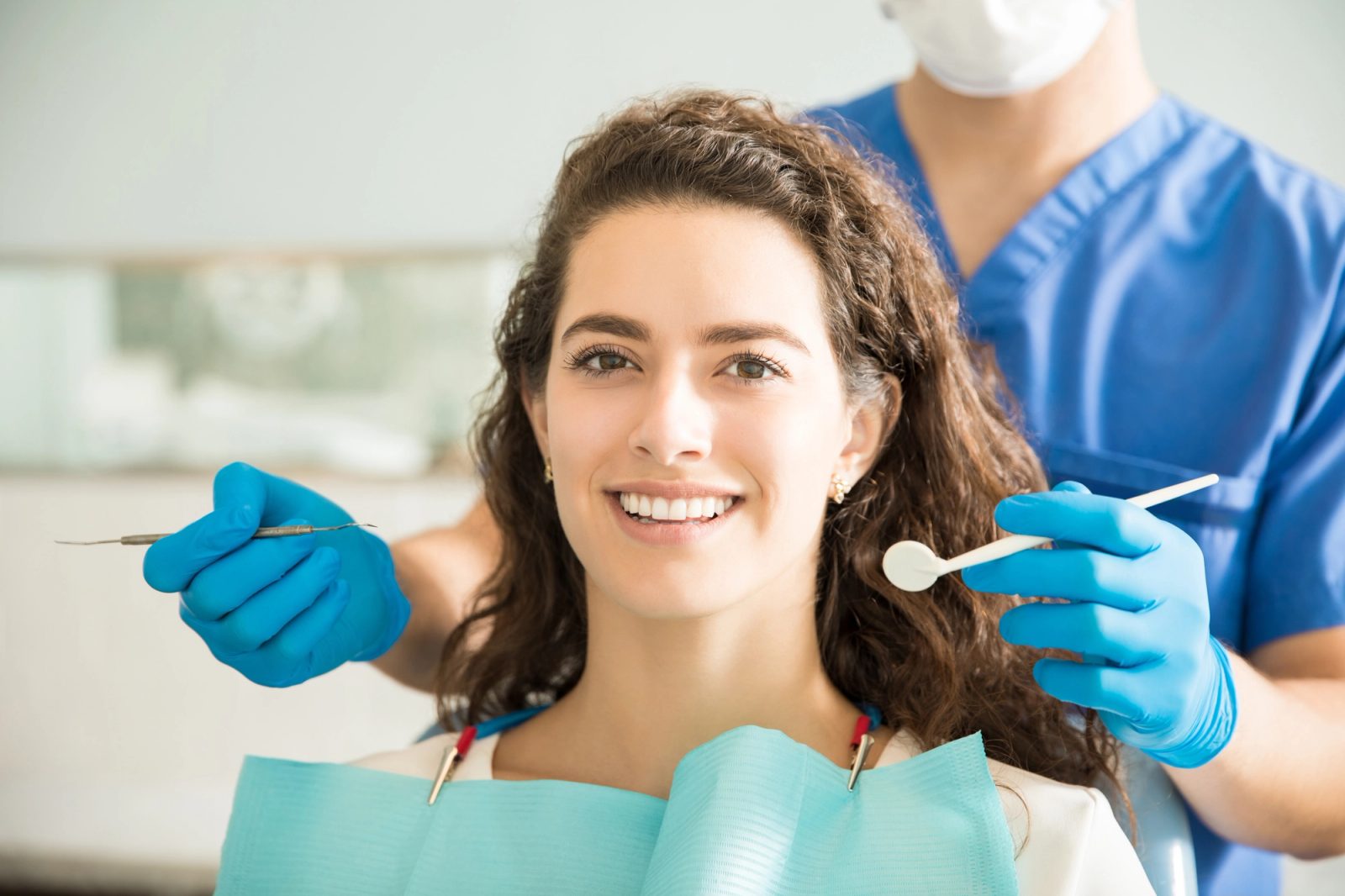 Smiling woman in a dental chair with a masked dentist holding tools.