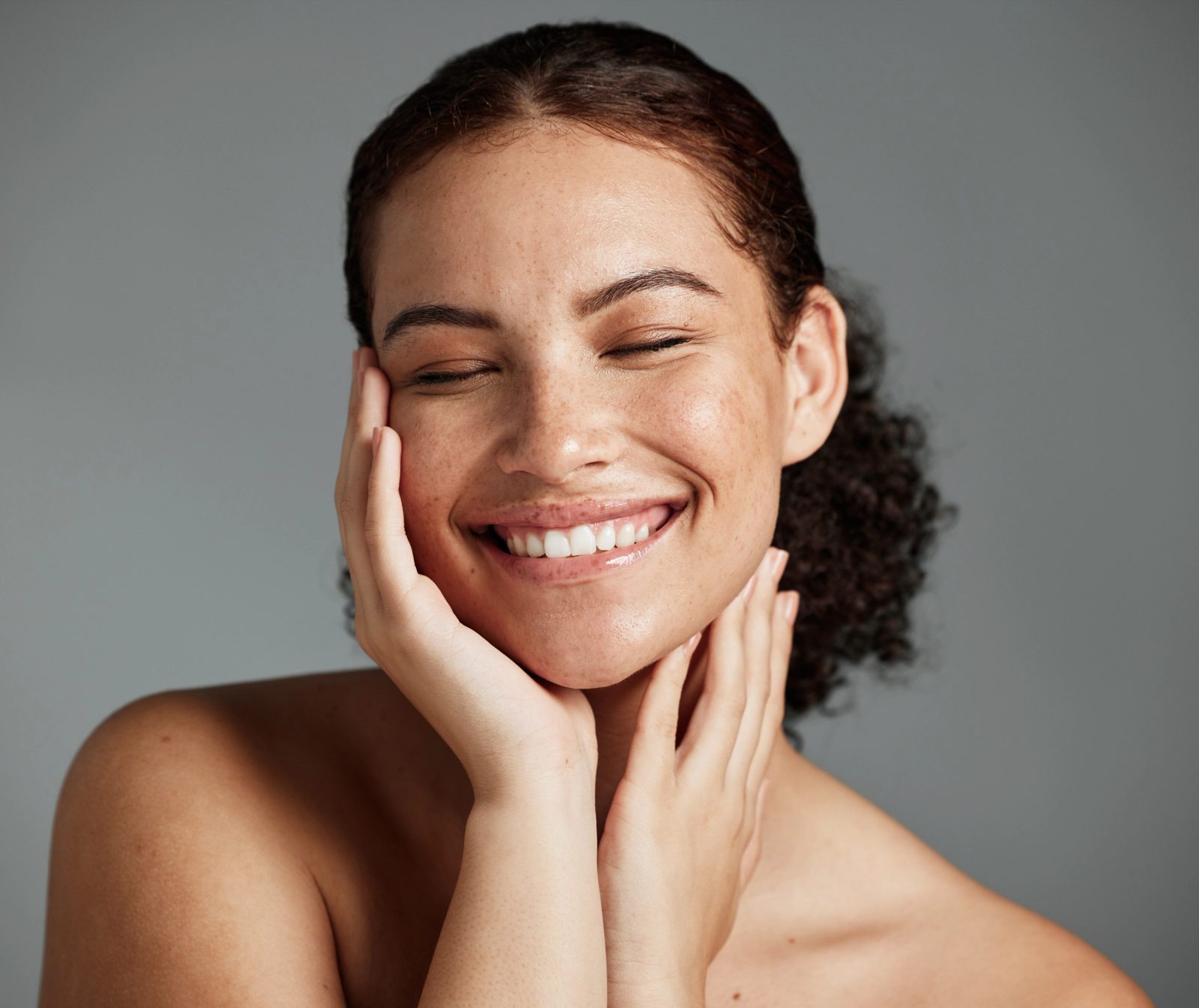 a woman is smiling and touching her face with her hands .