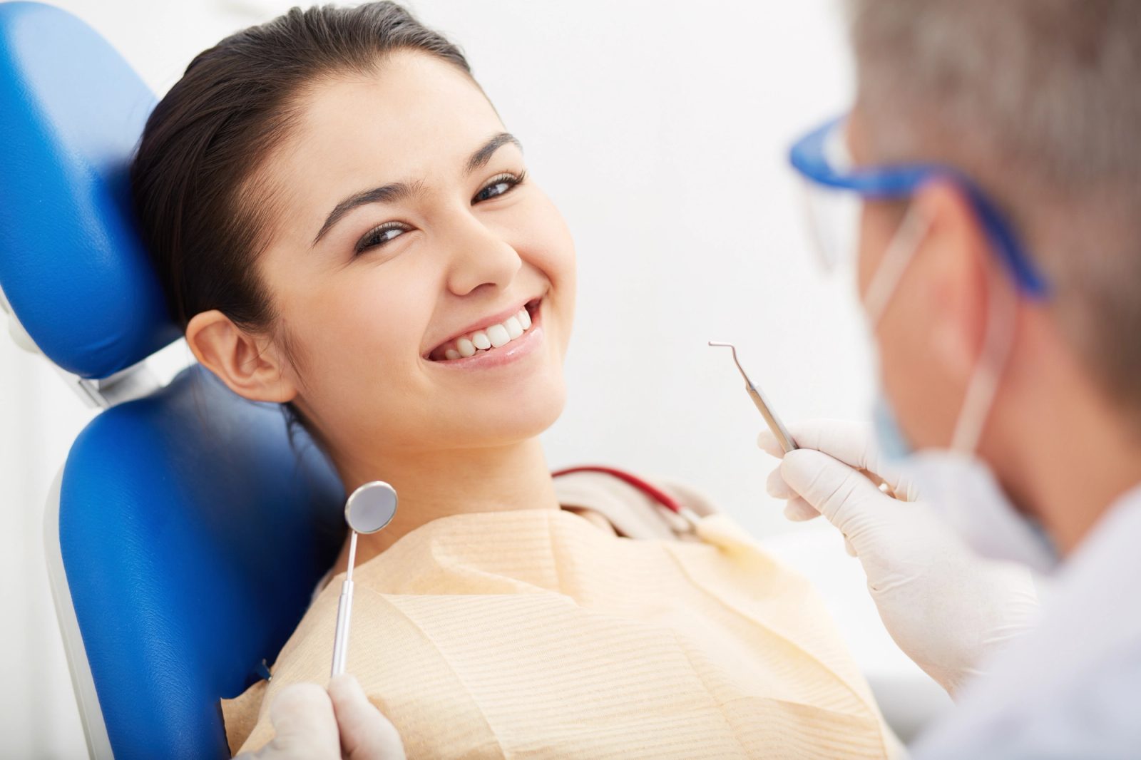 Young woman smiling in a dental chair while a dentist prepares to work.