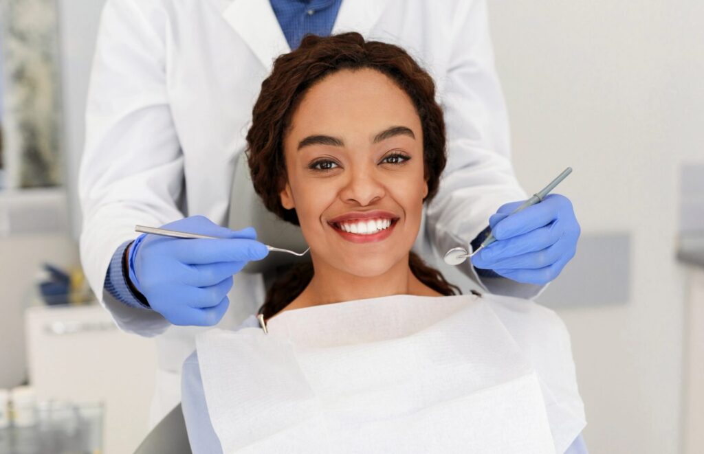 Smiling Black woman in a dental chair with a dentist holding dental tools.